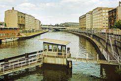 Blick von der Marschallbrücke entlang der Spree zum Bahnhof Friedrichstraße, an den Ufern (Schiffbauerdamm und Reichstagsufer) Sperranlagen mit Blech- und Stacheldrahtzäunen, links und in der Bildmitte: Abfertigungsgebäude der Grenzübergangsstelle "Marschallbrücke" für Lastenkähne. Bild 9138